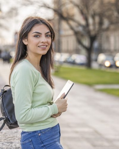 Student girl posing with a tablet in her hands near the river. Beauty in nature.